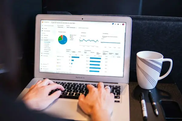 Hands typing on a laptop beside a coffee mug with a coordination of benefits dashboard on screen, representing Medicare Secondary Payer verification