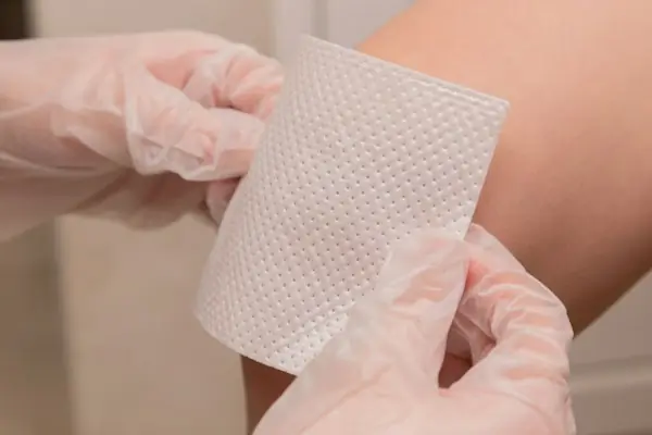 Gloved hands holding a sheet of wound dressing material, representing skin substitute application and billing