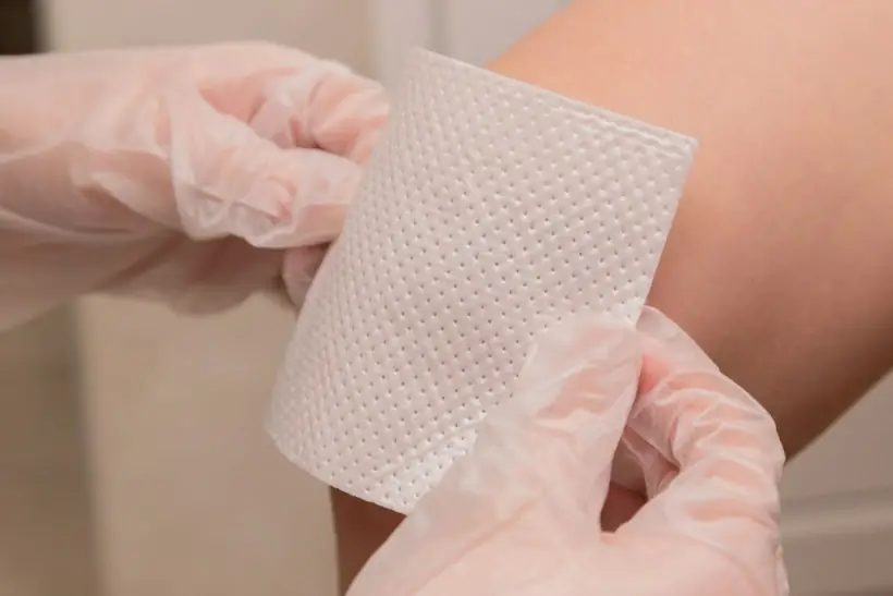 Gloved hands holding a sheet of wound dressing material, representing skin substitute application and billing