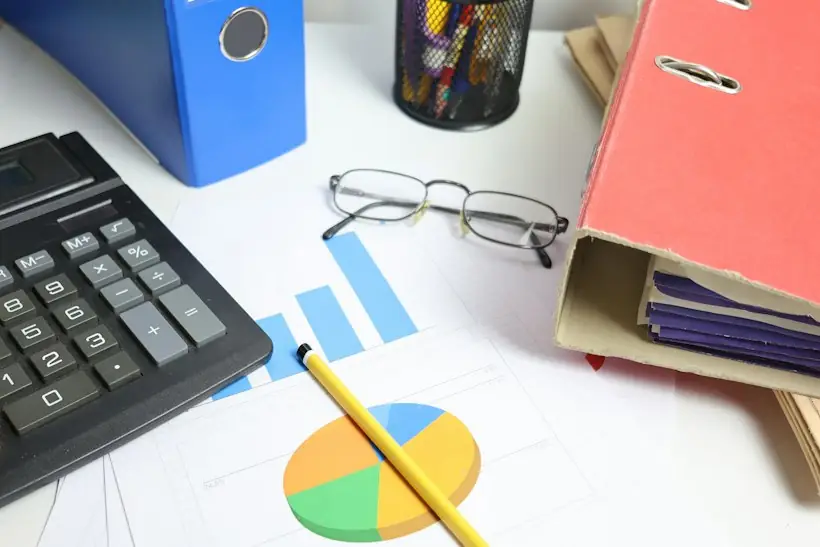 Calculator, binder and printed charts on a desk, representing overpayment reviews and credit balance reconciliation
